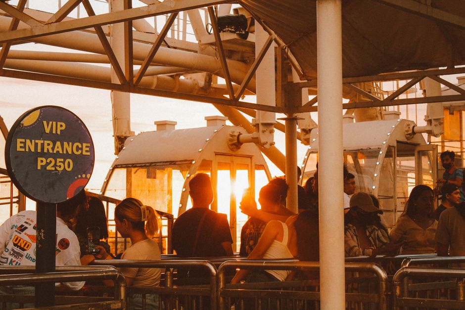 Tourists queuing for a ferris wheel ride at sunset with VIP entrance sign.
