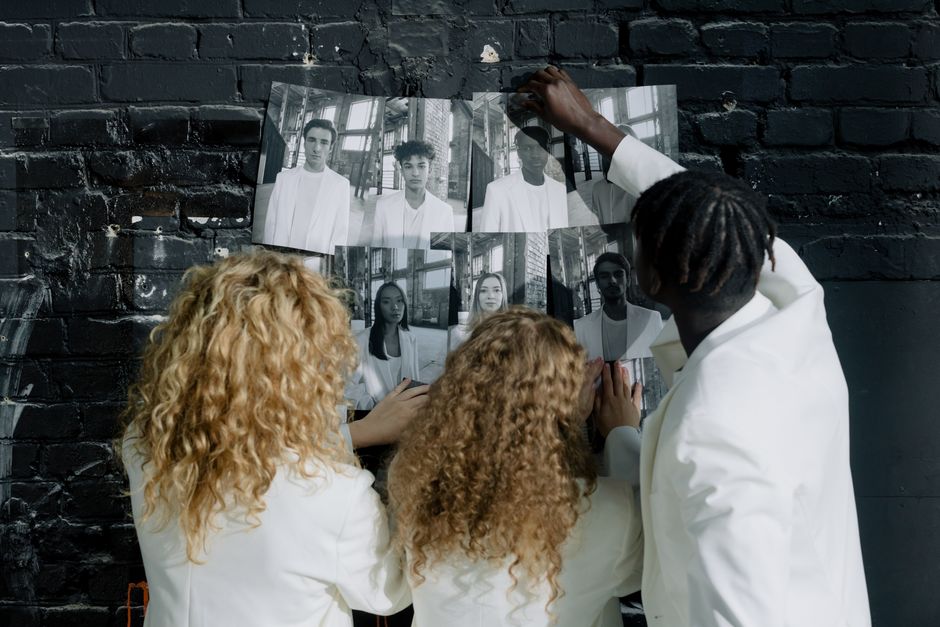 Three adults analyze black and white portraits on a brick wall promoting diversity and equality.